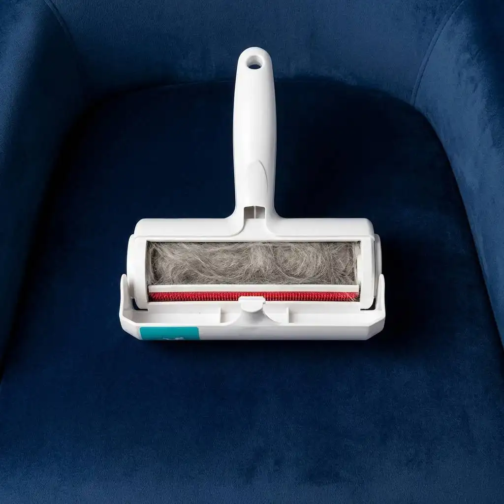 Open vacuum waste compartment filled with a dense roll of compressed grey cat hair on a navy blue velvet armchair.