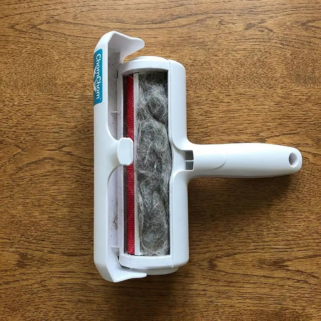 ChomChom roller on a wooden table with its waste compartment open to reveal a dense, compressed brick of trapped grey cat fur and dust.